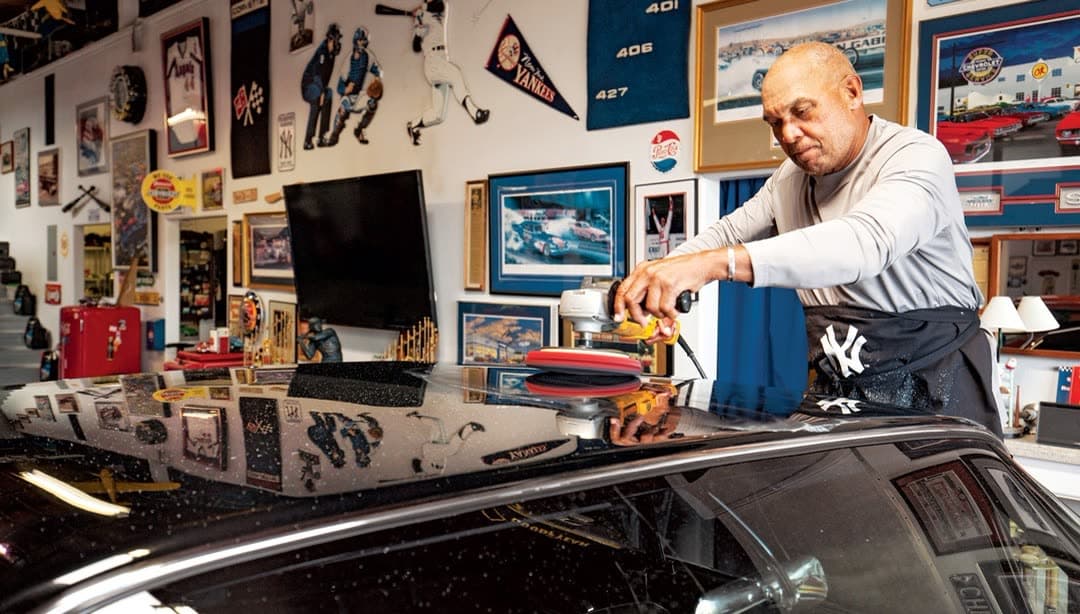 A car being hand-polished inside the garage, beneath a wall of baseball memorabilia
