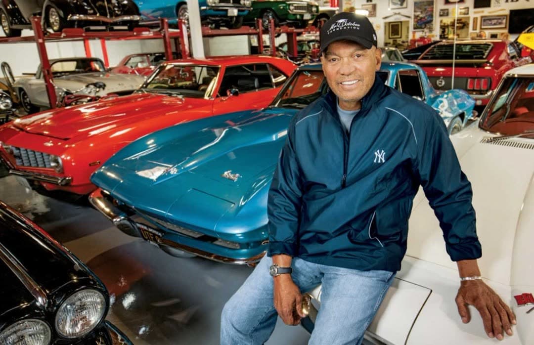 Reggie Jackson seated on a car inside his garage, with the collection behind him